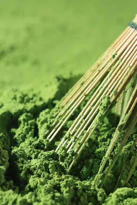 Bamboo broom stirring green powder on a green background
