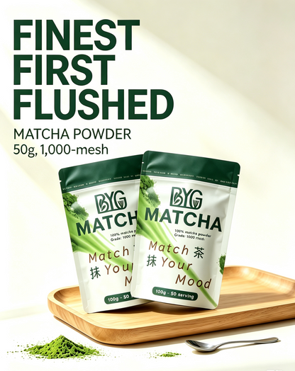 Two stand-up pouches of BYG Matcha powder displayed on a wooden tray with a spoon and loose green powder, under the text 'FINEST FIRST FLUSHED MATCHA POWDER 50g, 1,000-mesh'.