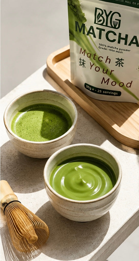 Two bowls of green matcha tea on a light stone surface with a wooden tray, a bamboo whisk, and a bag of BYG Matcha in the background.